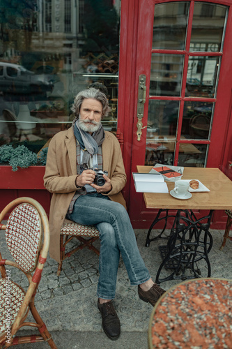 Elegant senior man with camera spending time at outdoor cafe