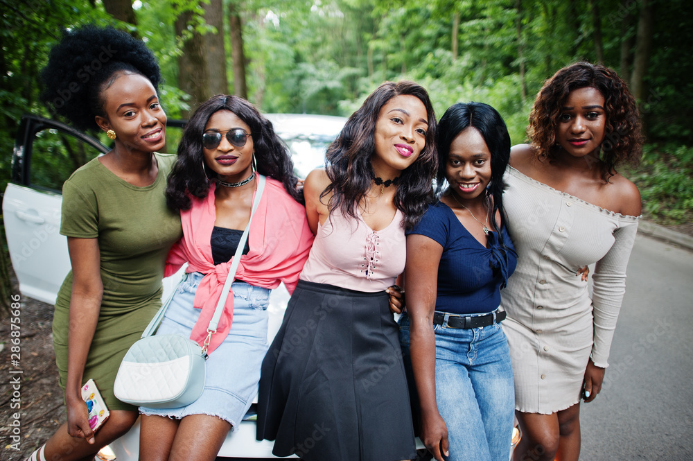 Group of five happy african american girls sitting on a car hood. Group of five happy african american girls sitting on a car hood.