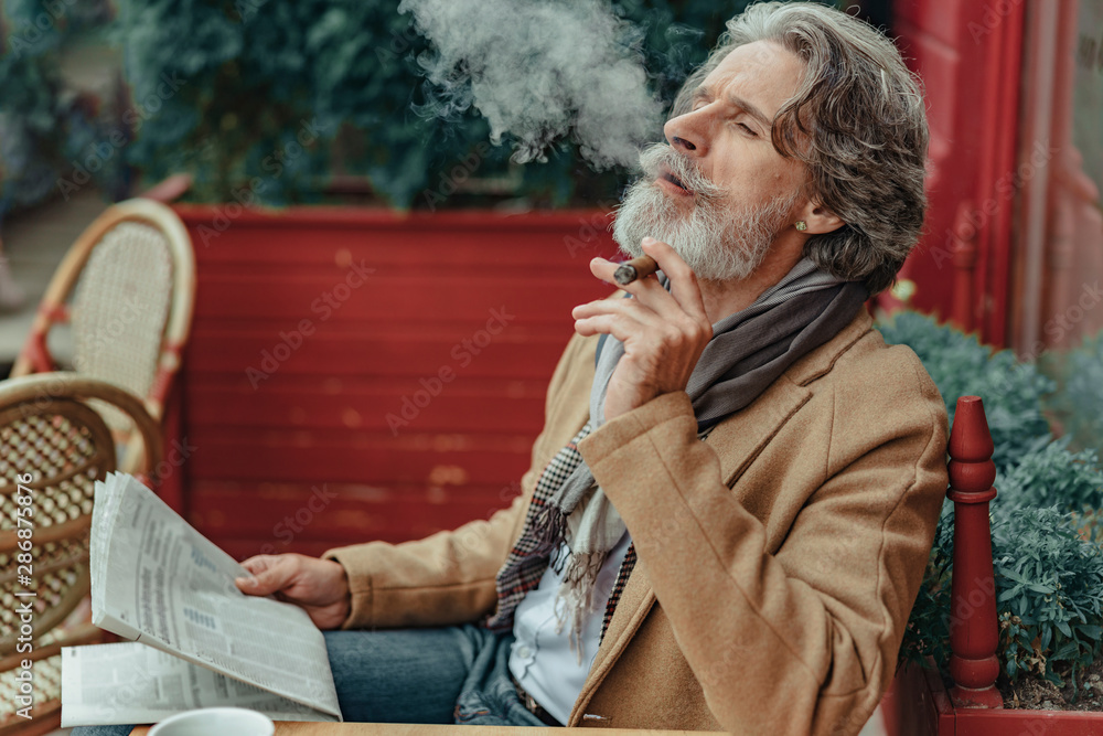 Obraz premium Elegant senior man blowing smoke out of his mouth