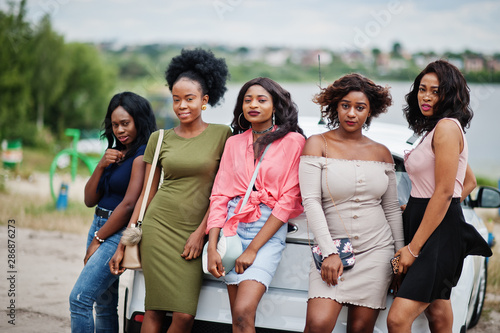 Group of five happy african american girls posed against car.