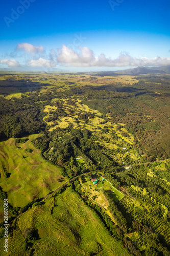 Aerial view of a lush tropical landscape with a road and a few small houses near Mauna Kea volcano
