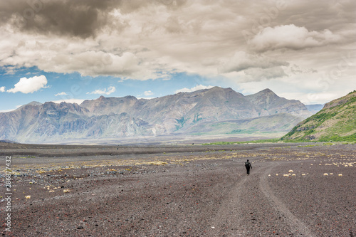 A young woman with backpack hiking on iceberg and snow and enjoying the views of the Antuco volcano black volcano desert. Northern Patagonia, Andes, Chile, South America. photo