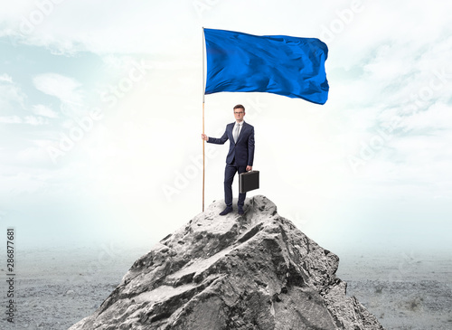 Handsome businessman on the top of the mountain with blue flag