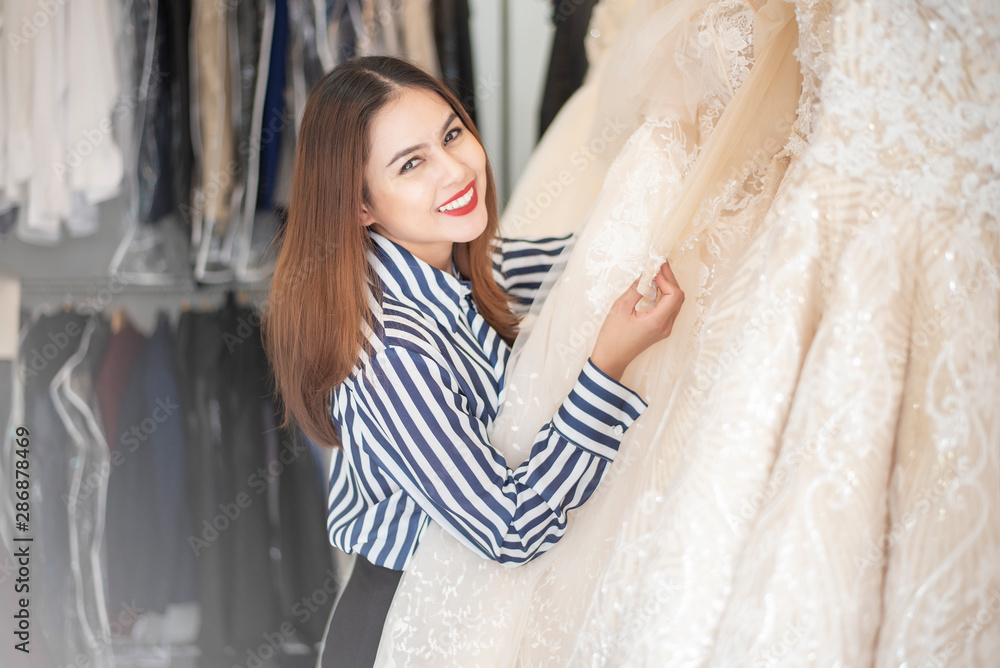 Fototapeta premium Beautiful woman is looking wedding dress in wedding shop