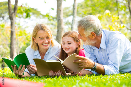 Happy Old Grandparents Having Fun With Grandchildren read a book In Park