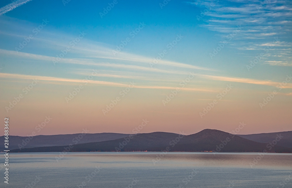 Dawn over the lake in the old mountains of the southern Urals. Fog above the water and among the wooded hills, colored by the rays of the rising sun
