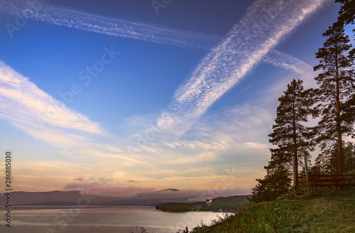 Picturesque landscape with a mountain lake  pine trees in the foreground  fog above the lake and among the mountains and a large sky with cirrus clouds