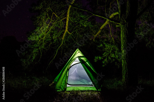Green tent in the forest at night. Camping with a tent in the forest
