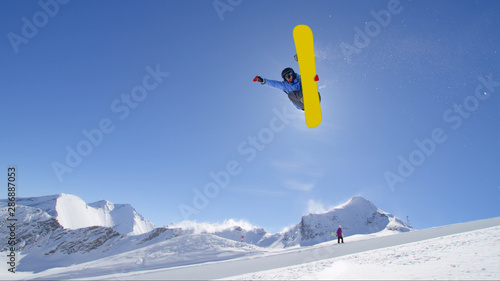 Fotografie Young pro snowboarder jumping in half pipe in sunny snow park