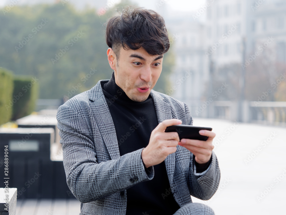Happy excited young man in suit using cell phone with funny expression, excited business man looking at his smart phone reading good news message email, emotional lifestyle concept. Happy excited young man in suit using cell phone with funny expression, excited business man looking at his smart phone reading good news message email, emotional lifestyle concept.