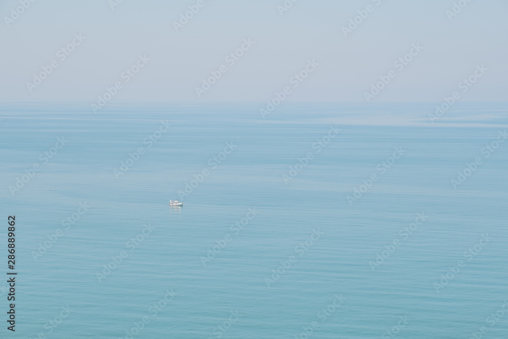 Calm blue sea fusing with skies.  Peaceful and tranquil marine view, a small boat passing by.