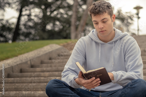 Christian worship and praise. A young man is praying and reading the bible in the evening.
