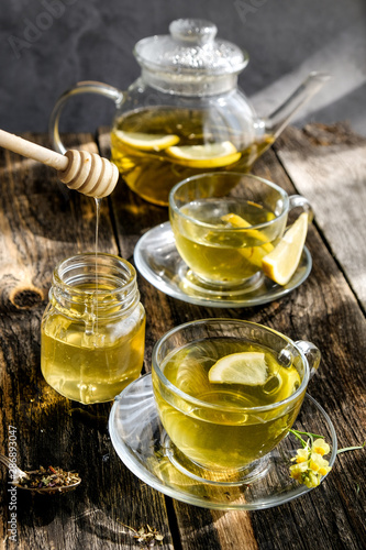 Herbal tea with lemon and honey in glass cup and teapot on sunny day light