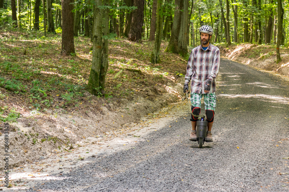 Obraz premium Men learns to ride a monowheel on a rural country road.