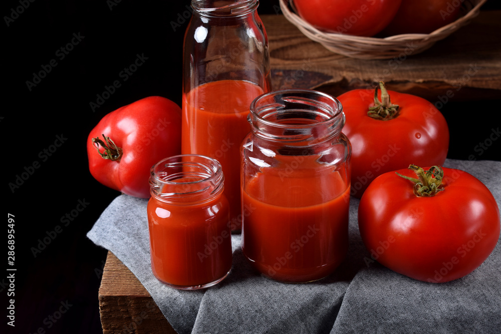 Tomato juice in glass jars on wooden table. Dark photo Tomato juice in glass jars on wooden table. Dark photo