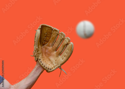 Photography Hand in a leather baseball glove catches a white ball in defocus on a red backgr