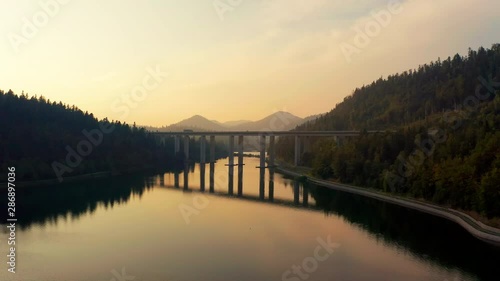 Aerial view of Bajer lake surrounded by hills and mountains with coniferous forest. Drone flying under the bridge at Bajer lake in Fuzine, Croatia. Nature background in 4K resolution.