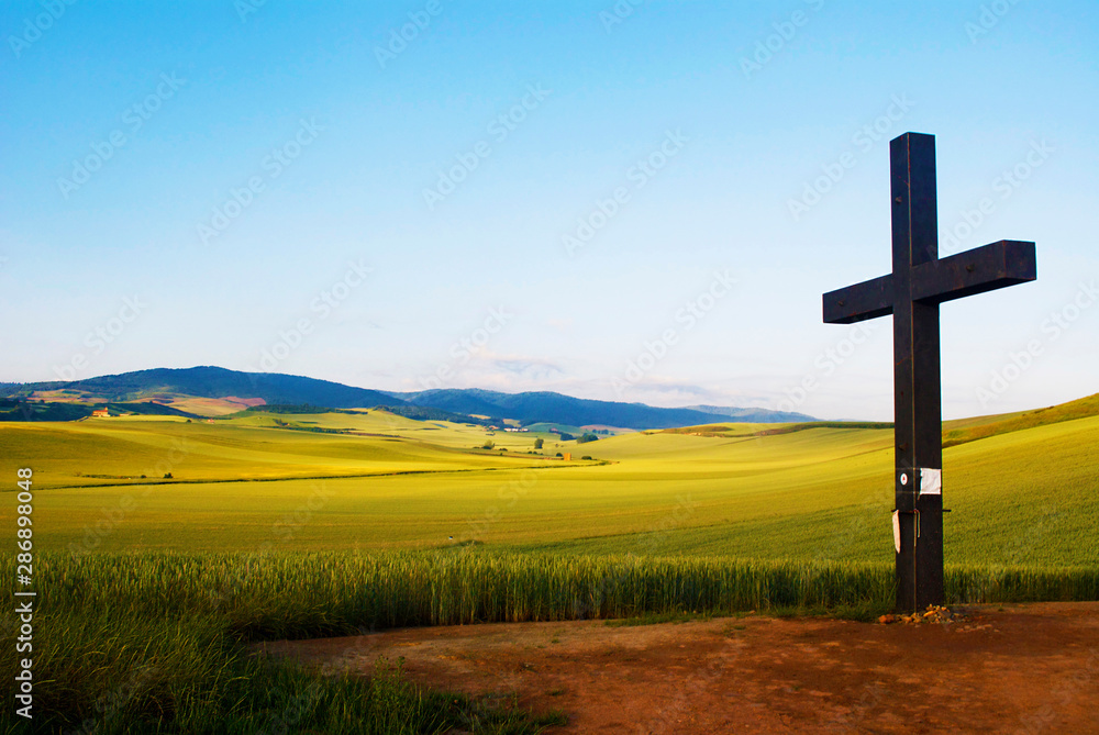 Large cross overlooking green valley and mountains.