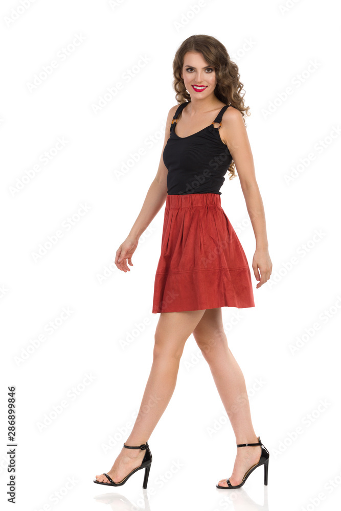 Young Woman In Brown Suede Mini Skirt And High Heels Is Walking And Looking At Camera. Side View. Young Woman In Brown Suede Mini Skirt And High Heels Is Walking And Looking At Camera. Side View.
