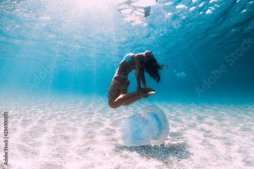 Woman diver glides over sandy sea with jellyfish. Freediving in blue ocean