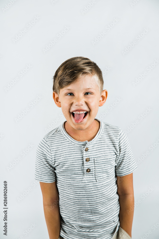 Little boy with autism standing on a white background feeling happy with tongue sticking out Little boy with autism standing on a white background feeling happy with tongue sticking out