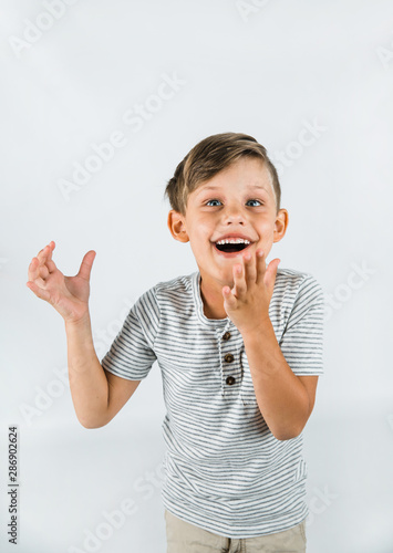 Little boy with autism standing on a white background feeling happy and smiling with his arms raised