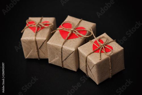 Set of gift boxes on black background. Heart cardboard. Parcels wrapped in craft paper and tie hemp cord.
