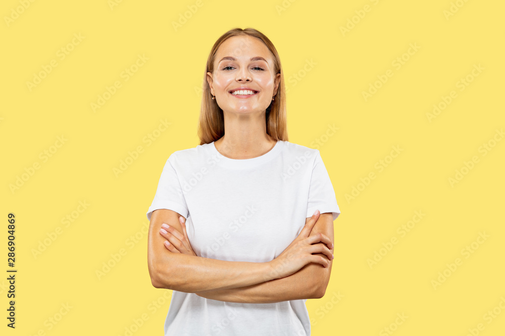 Caucasian young woman's half-length portrait on yellow studio background. Beautiful female model in white shirt. Concept of human emotions, facial expression, sales. Standing hands crossed, confident. Caucasian young woman's half-length portrait on yellow studio background. Beautiful female model in white shirt. Concept of human emotions, facial expression, sales. Standing hands crossed, confident.