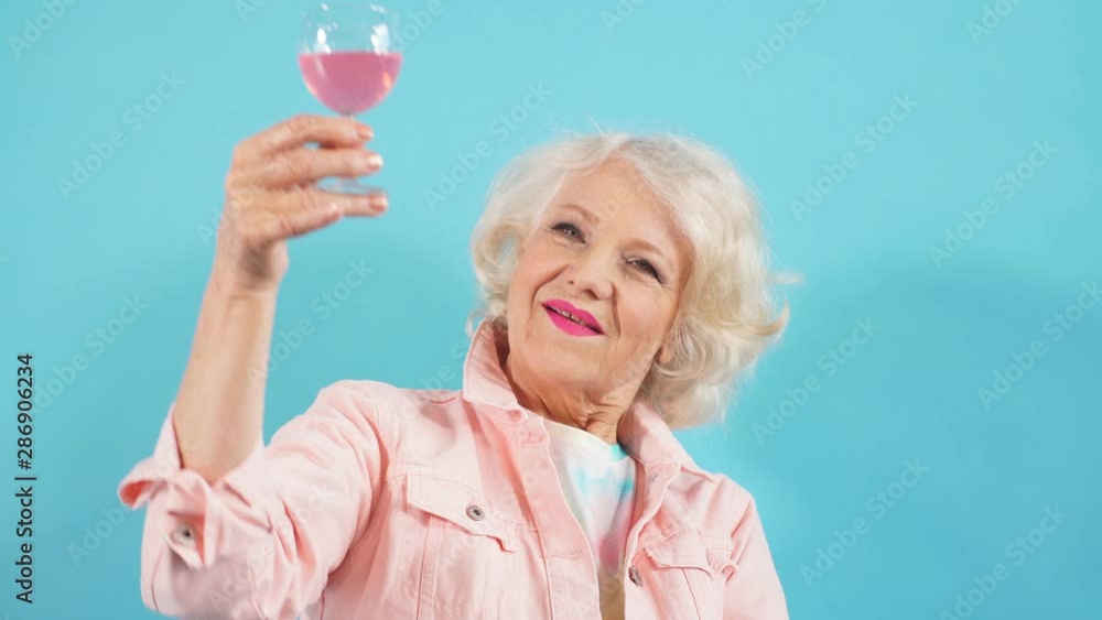 Happy positive grandma with glass looking at the camera, celebrating her birthday. Happiness, positive emotion and feeling. Isolated blue background Happy positive grandma with glass looking at the camera, celebrating her birthday. Happiness, positive emotion and feeling. Isolated blue background