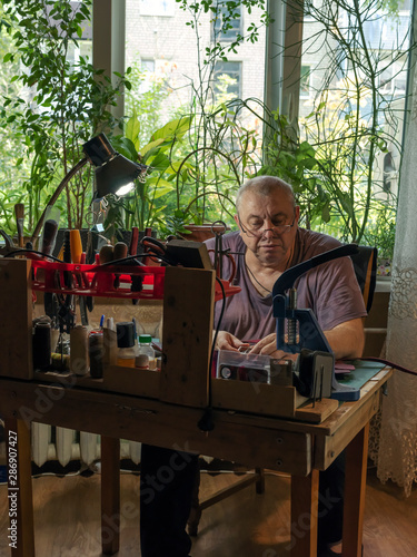 Middle-aged man with glasses sews leather goods in a workshop.