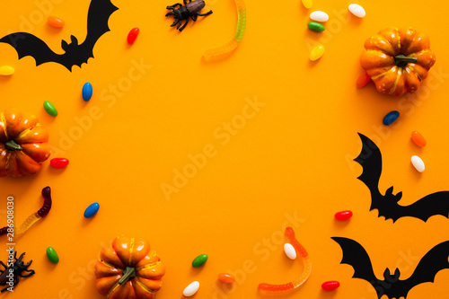 Happy halloween holiday concept. Halloween decorations, pumpkins, bats, candy, bugs on orange background. Halloween party greeting card mockup with copy space. Flat lay, top view, overhead.