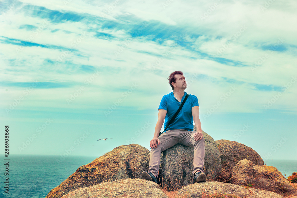 man sitting on a rock with his back to the sea thoughtful looking up