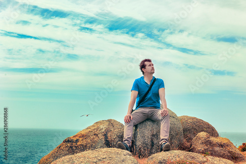 man sitting on a rock with his back to the sea thoughtful looking up