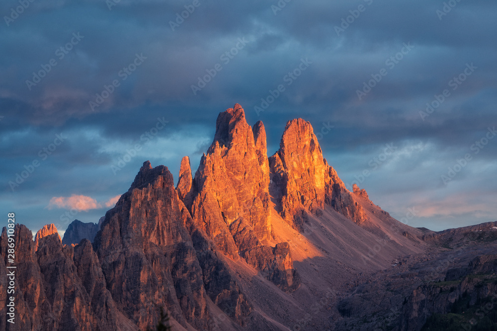 Golden glowing Cima Ambrizzola UNESCO Dolomites during sunset with dramatic dark sky and clouds