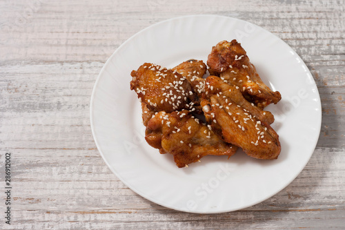 Fried juicy chicken wings marinated with honey, soy sauce, spices, sprinkled with sesame seeds on a white plate on a light background. Asian recipe, top view, close up