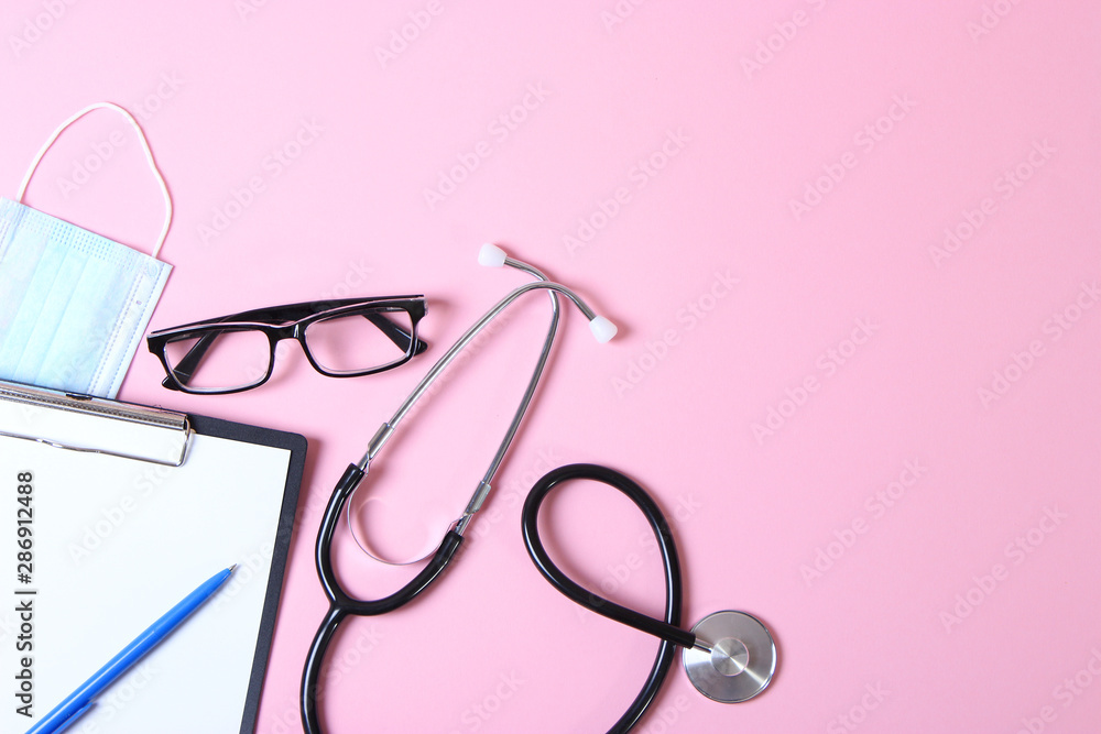 Fototapeta premium Doctor's desk top view. Stethoscope, pills, glasses and notebook on a colored background.