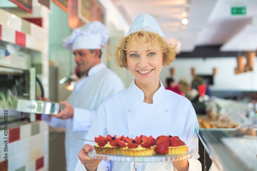 Portrait of smiling mature chef holding fresh strawberry tarts in tray at restaurant Portrait of smiling mature chef holding fresh strawberry tarts in tray at restaurant