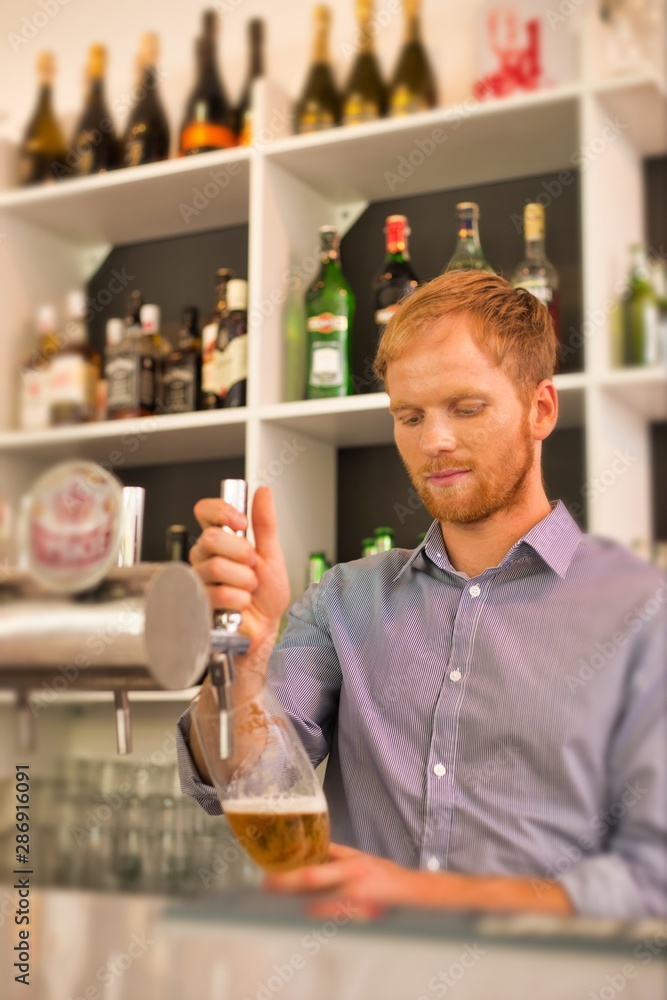 Young waiter filling glass from beer tap at restaurant