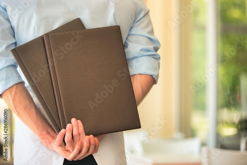 Rear view of young waiter holding menus while standing at restaurant © moodboard