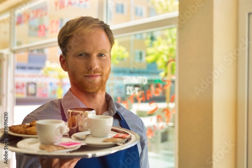 Young waiter serving coffee and cookies at restaurant