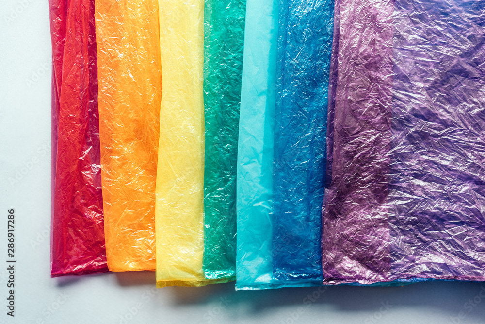 Naklejka premium Plastic bags in a row by the colors of the rainbow on gray background. The concept of recyclable household and industrial waste.