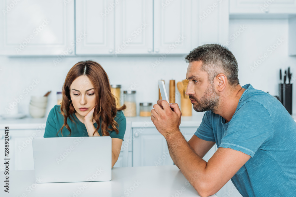 husband and wife sitting at kitchen table and using smartphones husband and wife sitting at kitchen table and using smartphones