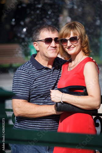 Middle-aged couple smiling and hugging on a walk in a public park, on the background of the fountain, selective focus