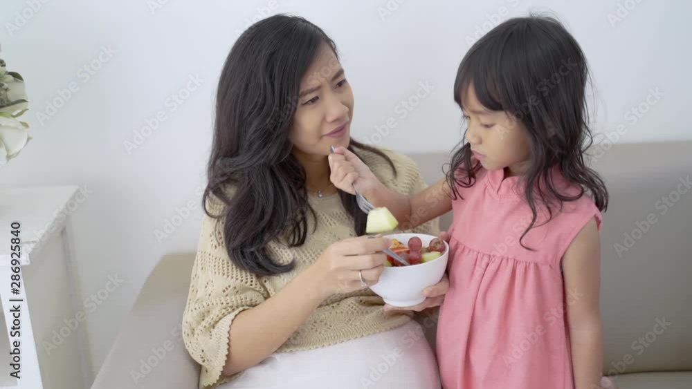 Pregnant mother and daughter eating salad together when sitting on couch Pregnant mother and daughter eating salad together when sitting on couch