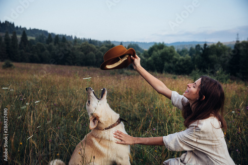 Girl and her friend dog are playing with a hat on the straw field background. Beautiful young woman relaxed and carefree enjoying a summer sunset with her lovely dog photo