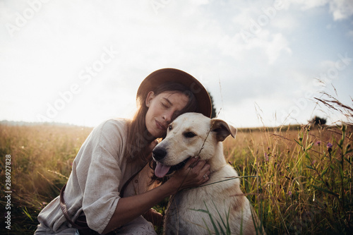 Beautiful young woman relaxed and carefree enjoying a summer sunset with her lovely dog on the straw field background