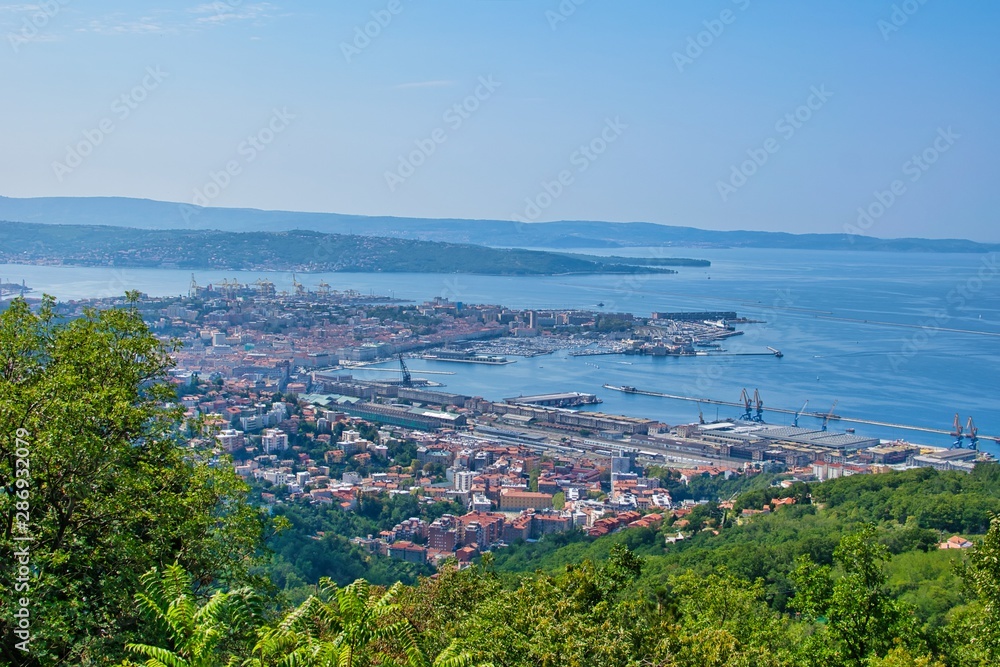Italy city - Trieste industrial area with red buildings and port. Sea and mountains in the background.Panoramic aerial view.