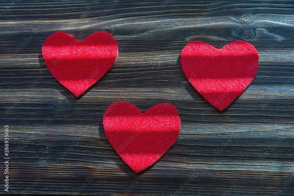 Handmade hearts from red felt with strips of light on dark rustic background. Flat lay Handmade hearts from red felt with strips of light on dark rustic background. Flat lay