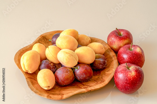 Apricots, plums and three apples on a wooden plate