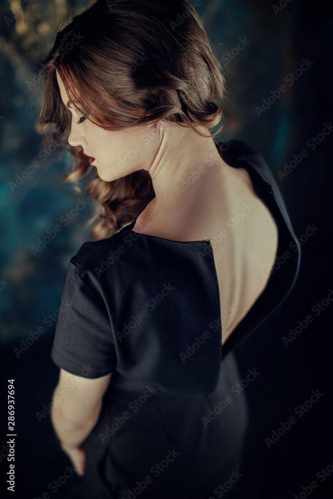 Portrait of young beutiful girl with brown curly hair, weared in black dress,stylish makeup. Studio shot